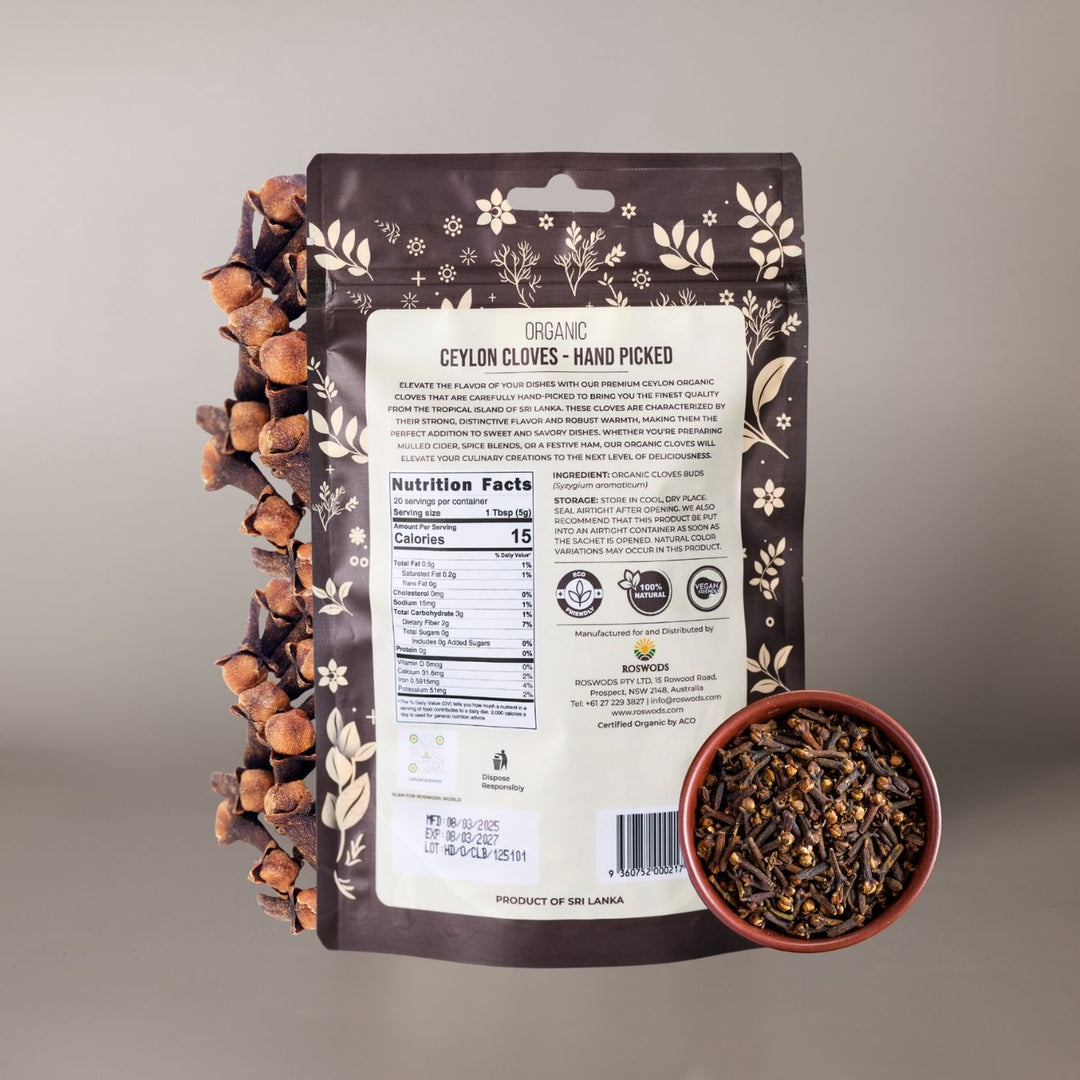 Back of Roswods Organic Ceylon Cloves bag showing Nutrition Facts panel, ingredient (Organic Cloves Buds - Syzygium aromaticum), storage instructions, and Eco Friendly, 100% Natural, and Vegan Natural badges. Product of Sri Lanka. Bag displayed with loose cloves and a small bowl of cloves on a warm grey background.