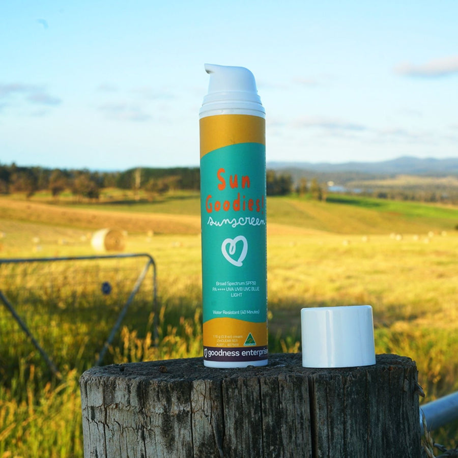 Sun Goodies! vegan SPF50 sunscreen in teal and yellow packaging on a wooden post, Australian-made organic sun protection in a rural field.