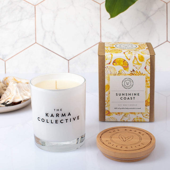 The Karma Collective Sunshine Coast Soy Wax Candle in an elegant white glass jar with a wooden lid. A warm, sweet scent with ethically sourced ingredients. 50% of each Karma Collective premium soy candle's profits are donated to World Animal Protection Australia, making it a perfect eco-friendly gift.
