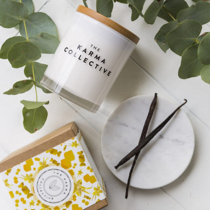 The Karma Collective Vanilla & Caramel Soy Wax Candle in an elegant white glass jar with a wooden lid. A warm, sweet scent with ethically sourced ingredients. 50% of each Karma Collective premium soy candle's profits are donated to World Animal Protection Australia.