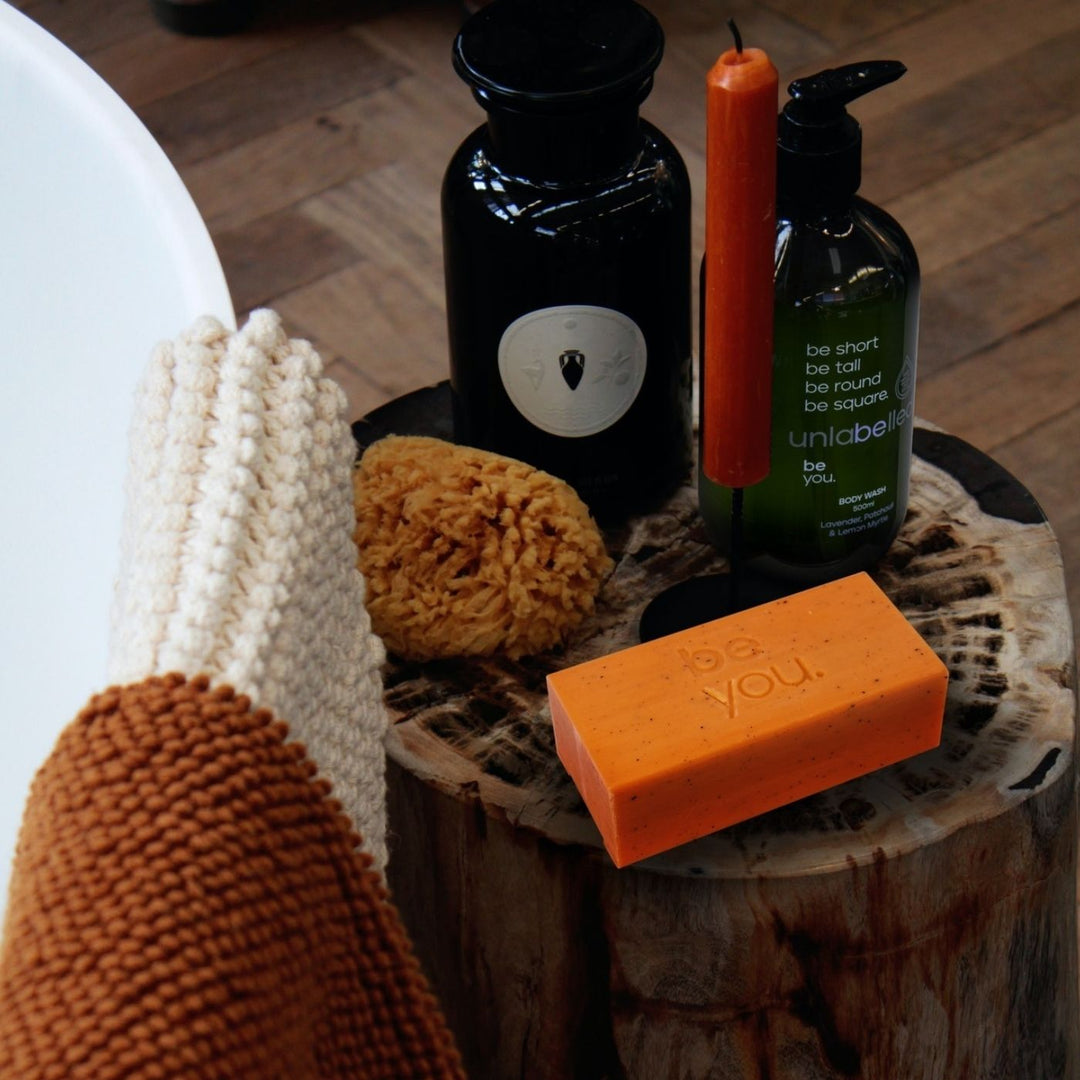 Unlabelled orange mandarin exfoliating body bar in bathroom setting, natural collagen soap for glowing skin, ethical Australian body care supporting youth mental health