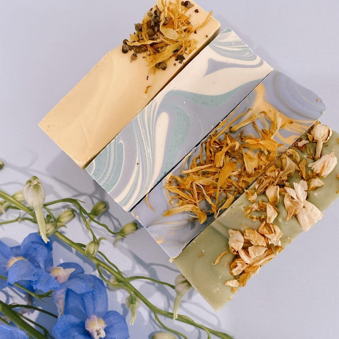 Artisan Sleepy Time soap bars scented with lavender, sweet orange and marjoram, displayed with dried botanicals on a soft blue background.
